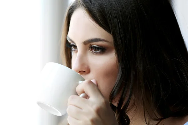 Женщина пьет кофе у окна в комнате — стоковое фото