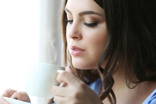 Mujer bebiendo café cerca de la ventana en la habitación —  Fotos de Stock