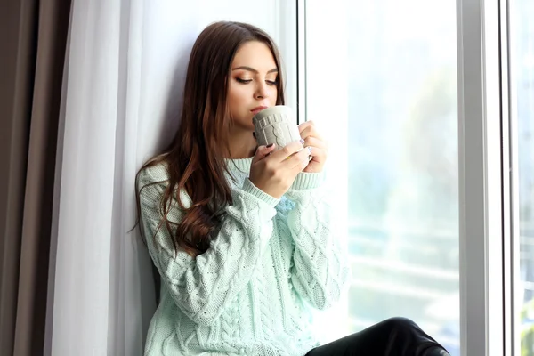 Mujer bebiendo café cerca de la ventana en la habitación — Foto de Stock