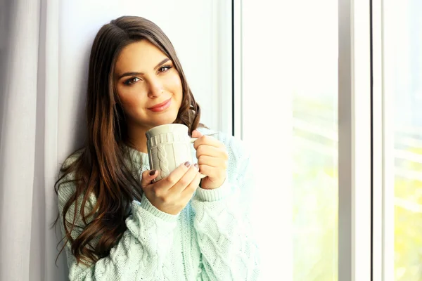 Mujer bonita sentada en el tablero de la ventana con una taza de café — Foto de Stock