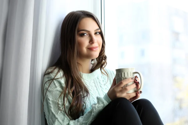 Ładna kobieta siedzi w zarządzie okno z filiżanką kawy — Zdjęcie stockowe