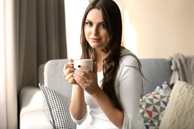 Güzel bir fincan kahve ile odasında kanepede rahatlatıcı kadın