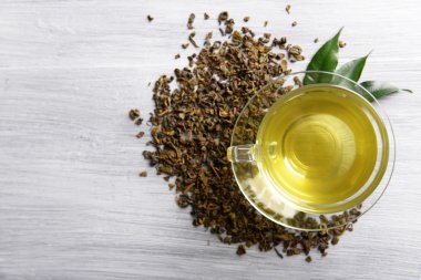 Cam bardak çay yeşil yaprakları ile ve gri ahşap arka plan üzerinde etrafında dağınık çay yakın çekim