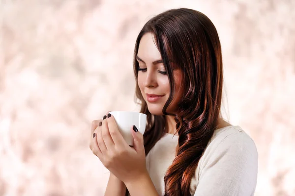 Портрет улыбающейся красивой женщины с чашкой кофе на розовом размытом фоне — стоковое фото