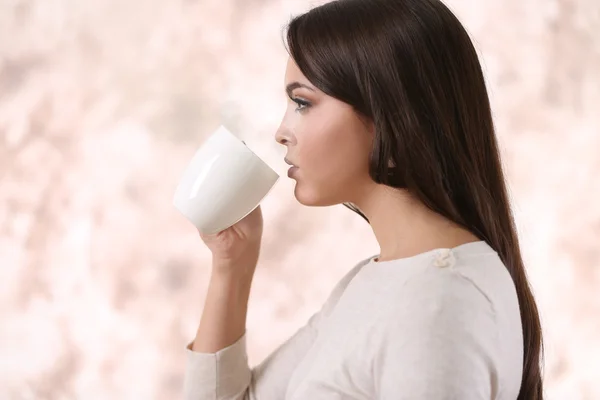 Beautiful young woman drinking coffee on pink blurred background — Stock Photo, Image