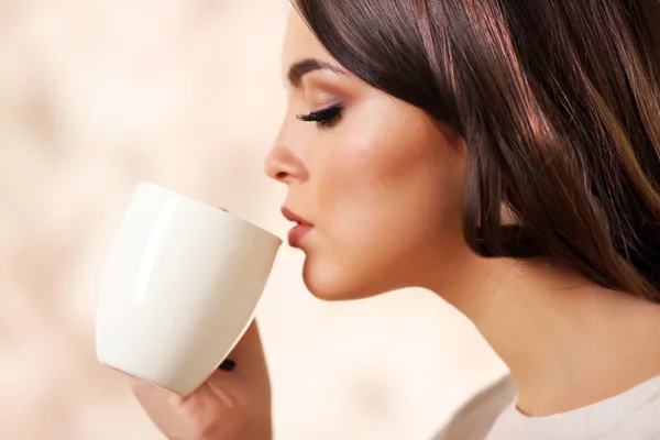 Beautiful young woman drinking coffee on pink blurred background — Stock Photo, Image