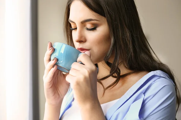 Mujer con taza de café de pie cerca de la ventana en la habitación — Foto de Stock