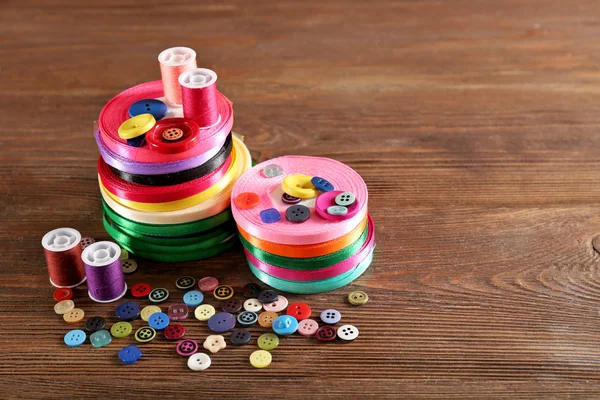 Spools of color ribbon and buttons on wooden background — Stock Photo, Image