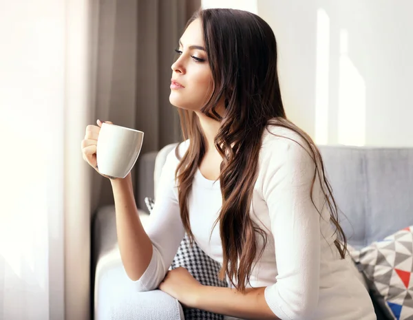 Hermosa mujer relajándose en el sofá en la habitación con una taza de café — Foto de Stock