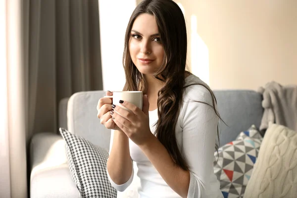 Mulher bonita relaxando no sofá no quarto com xícara de café — Fotografia de Stock