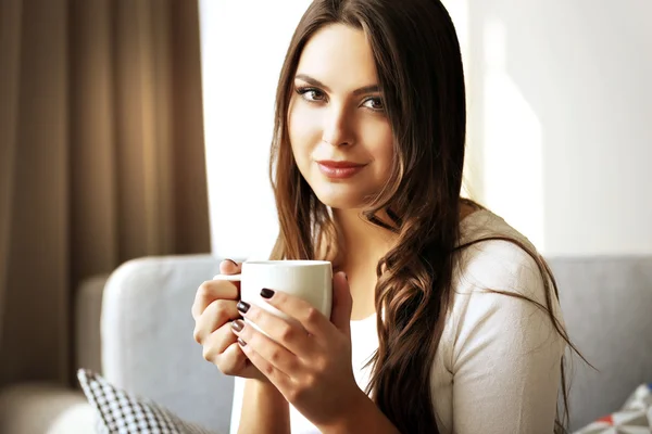 Mulher bonita relaxando no sofá no quarto com xícara de café — Fotografia de Stock