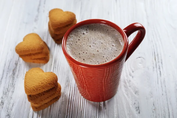 Red cup of hot cacao and heart shaped cookies on wooden background — Stock Photo, Image