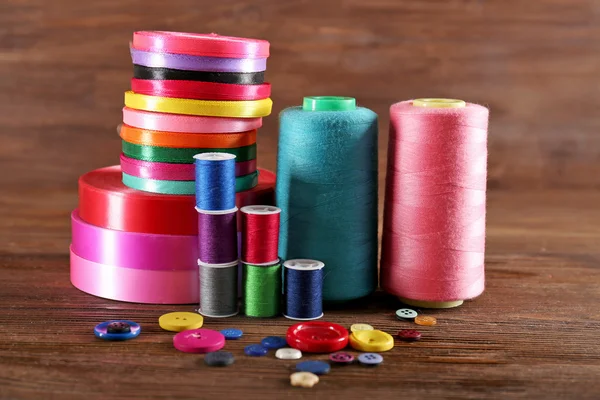 Spools of color ribbon, thread and buttons on wooden background — Stock Photo, Image