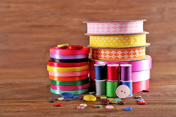 Spools of color ribbon, thread and buttons on wooden background — Stock Photo, Image