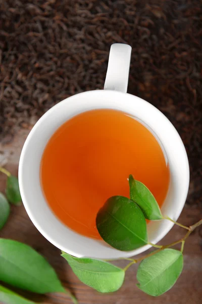 Ceramic cup of tea with scattered tea leaves around on wooden background