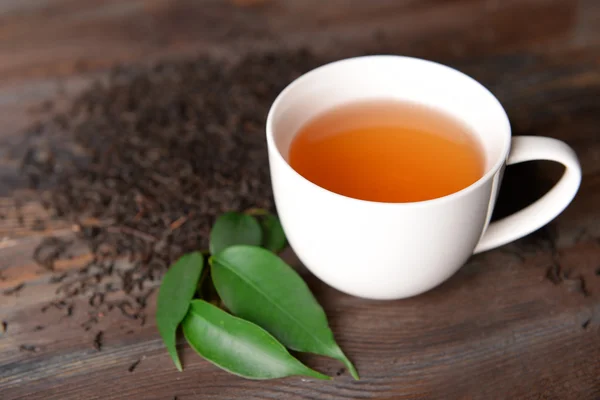 Taza de té de cerámica con hojas de té dispersas sobre fondo de madera — Foto de Stock