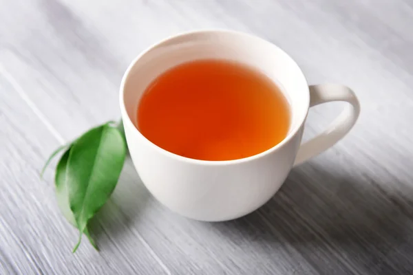 Kerámia csésze tea, zöld levelek, világos fából készült háttér — Stock Fotó
