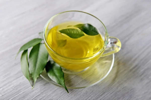 Glass cup of tea with green leaves on grey wooden background — Stock Photo, Image