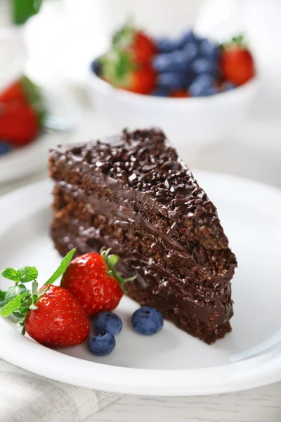 Шоколадний торт з шоколадним кремом і свіжими ягодами на тарілці, на світлому фоні — стокове фото