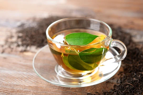Copa de té de vidrio con hojas verdes sobre fondo de madera decorado con té disperso — Foto de Stock