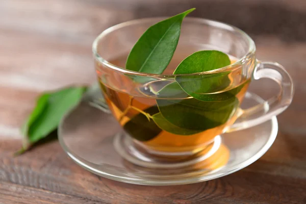 Coupe de thé en verre avec des feuilles vertes sur fond en bois — Photo