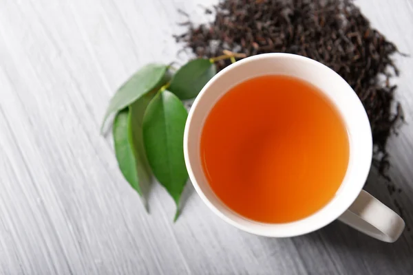 Keramische kopje thee met verspreide thee bladeren rond op lichte houten achtergrond — Stockfoto