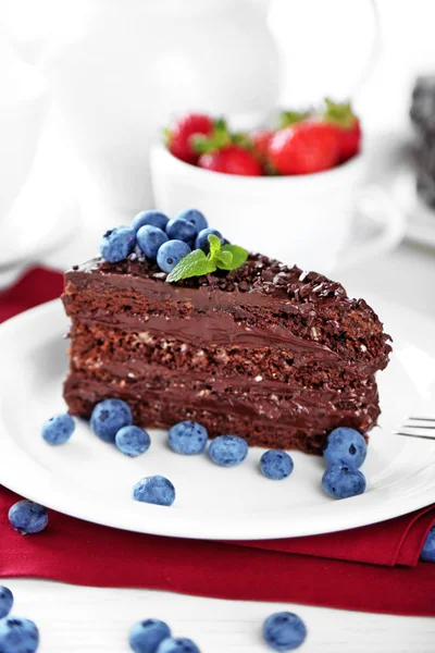 Chocolate cake met chocolade en verse bessen op plaat, op houten tafel, op lichte achtergrond — Stockfoto