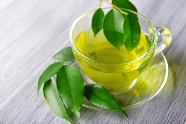 Glass cup of tea with green leaves on grey wooden background — Stock Photo, Image