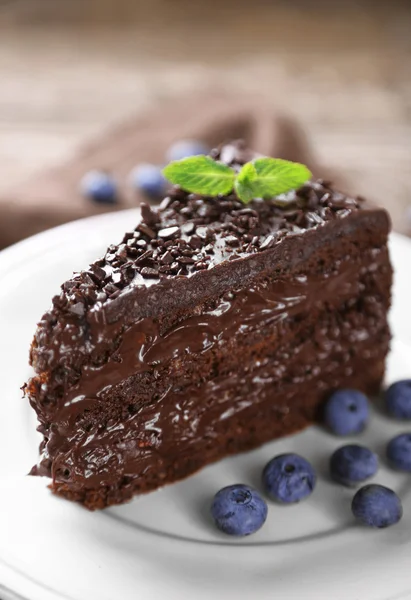 Chocolate cake with chocolate cream and fresh blueberries on plate, on wooden background — Stock Photo, Image