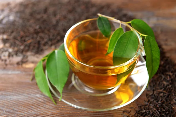 Copa de té de vidrio con hojas verdes sobre fondo de madera decorado con té disperso — Foto de Stock
