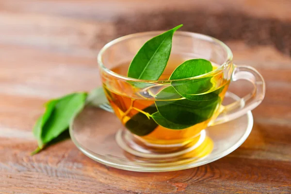 Coupe de thé en verre avec des feuilles vertes sur fond en bois — Photo