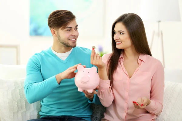 幸せなカップルが家で座っていると、豚の貯金箱からお金を数える — ストック写真