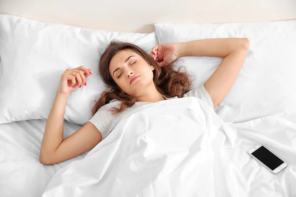 Vacker ung kvinna som vaknar upp med mobila väckarklocka — Stockfoto