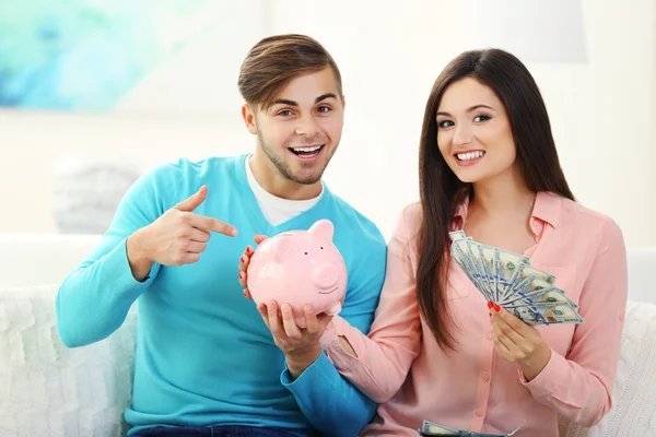 Casal feliz sentado em casa e contando dinheiro da caixa de dinheiro porco — Fotografia de Stock