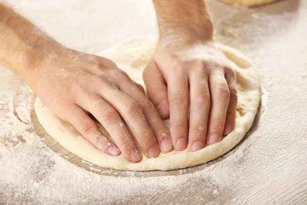 Mãos preparando base de massa para pizza na mesa de madeira, close-up — Fotografia de Stock