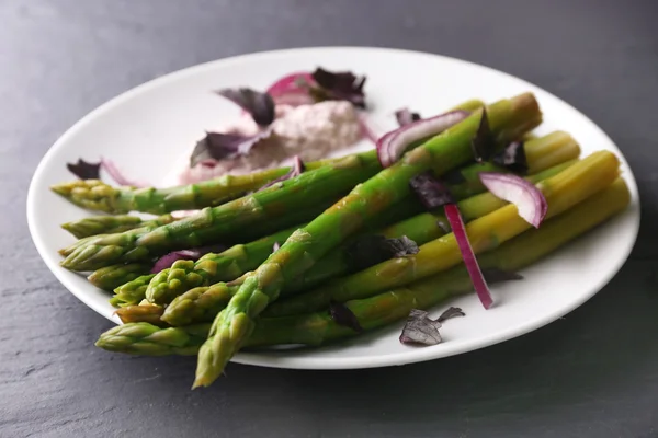 Verse asperges schotel met rode gehakte ui op wit bord tegen grijze houten achtergrond, close-up — Stockfoto