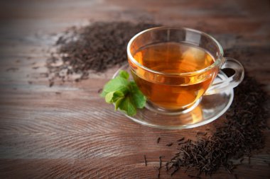 Dağınık çay ile dekore edilmiş ahşap arka plan üzerinde cam bardak yeşil çay yaprakları