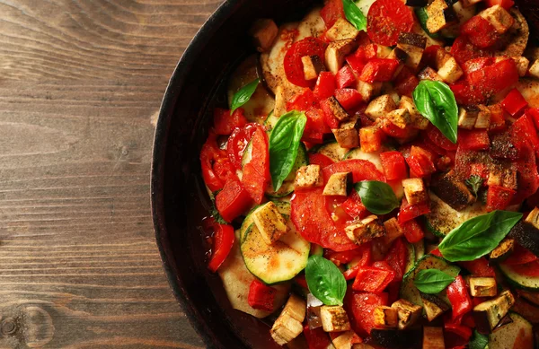 Tasty vegetarian ratatouille made of eggplants, squash, tomatoes and onions in black cast iron pan, on wooden table background — Stock Photo, Image