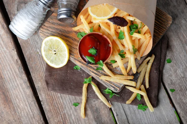 Batatas fritas francesas em papel artesanal na tábua de corte — Fotografia de Stock