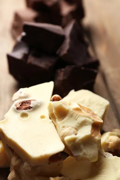 Pedaços de chocolate preto, leite e branco na cor de fundo de madeira — Fotografia de Stock