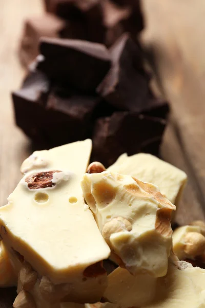 Black, milk and white chocolate pieces on color wooden background — Stock Photo, Image