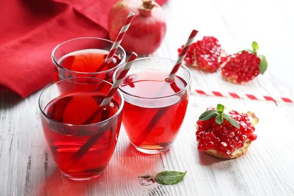 Three glasses of tasty juice and garnet fruit, on wooden background — Stock Photo, Image