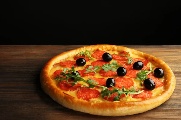 Pizza saborosa com salame e azeitonas na mesa de madeira contra fundo preto — Fotografia de Stock