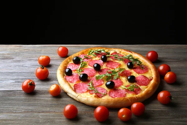 Smakelijke pizza salami en olijven versierd met tomaten op houten tafel tegen zwarte achtergrond — Stockfoto