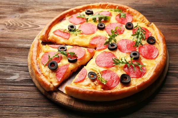 Pizza gostosa quente com salame e azeitonas em fundo de madeira — Fotografia de Stock