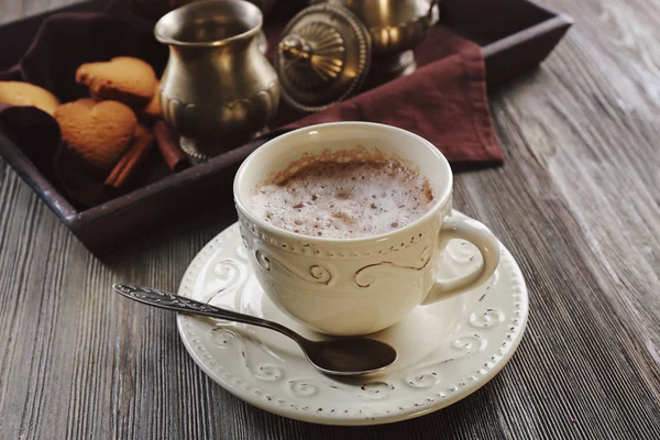 Vintage cup of cacao on wooden table against tray with silver service and cookies