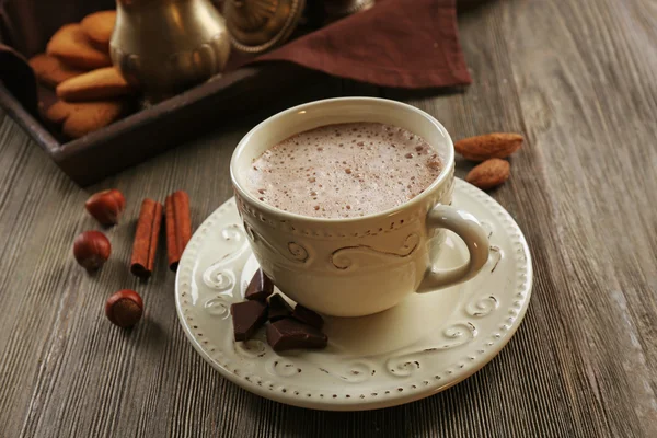 Старовинна чашка какао на дерев'яному столі проти лотка зі срібною службою та печивом — стокове фото