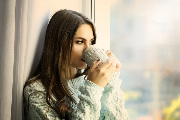 Женщина пьет кофе у окна в комнате — стоковое фото
