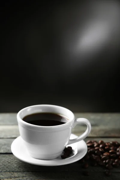Filiżankę kawy i ziarna kawy na drewnianym stole, na szarym tle — Zdjęcie stockowe