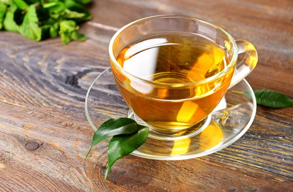 Glass cup of tea with green leaves on wooden background — Stock Photo, Image